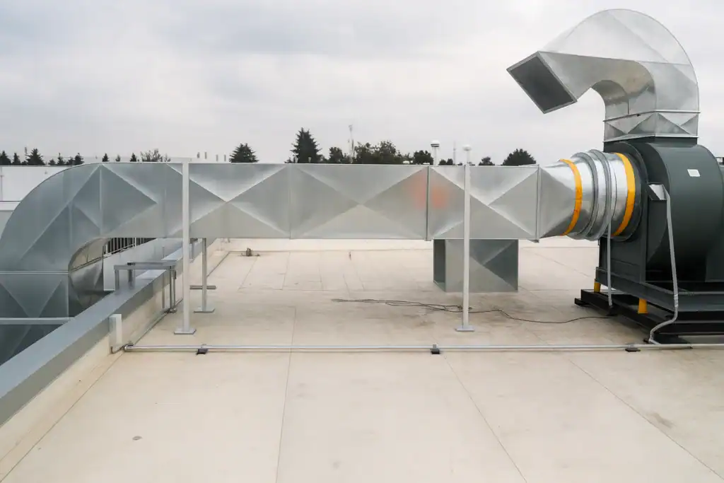 Ventilador centrífugo industrial en azotea con ductos galvanizados rectangulares y transición a redondo — sistema de extracción MCAT