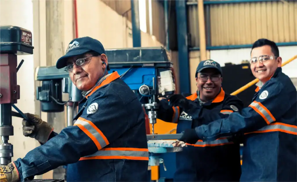 Equipo técnico de MCAT en taller con taladro de columna y EPP — fabricación e instalación de ventilación industrial