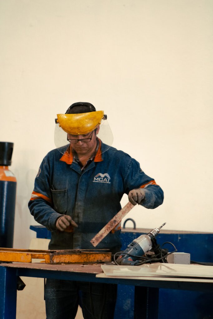 Técnico de MCAT realizando medición y ensamble en taller; fabricación de componentes para ventilación industrial con equipo de protección personal
