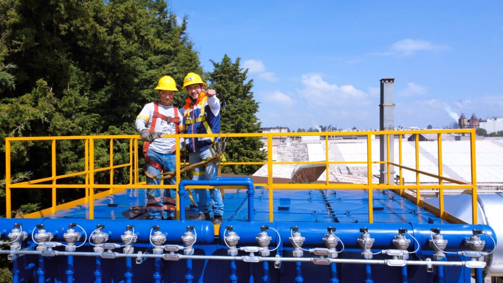 Técnicos con arnés y casco realizando inspección en altura sobre colector de polvos; instalación y mantenimiento de ventilación industrial en planta
