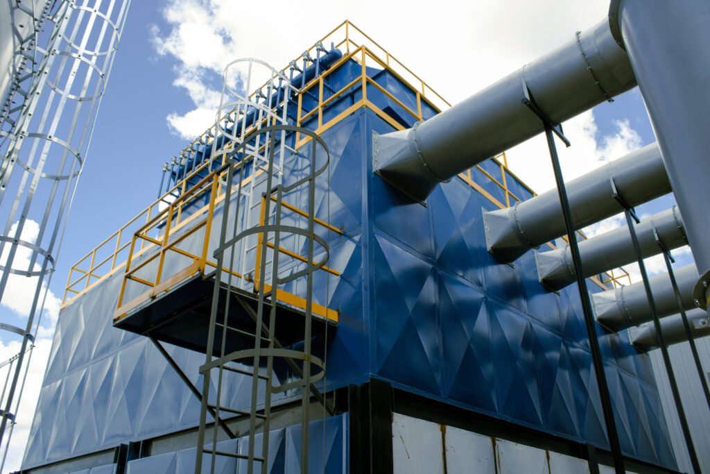 Colector de polvos industrial tipo baghouse con ductería y múltiples entradas; sistema de extracción de partículas en planta con plataforma de mantenimiento